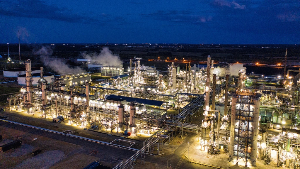 Industrial plant illuminated at night, showing processing equipment, towers, and site lighting