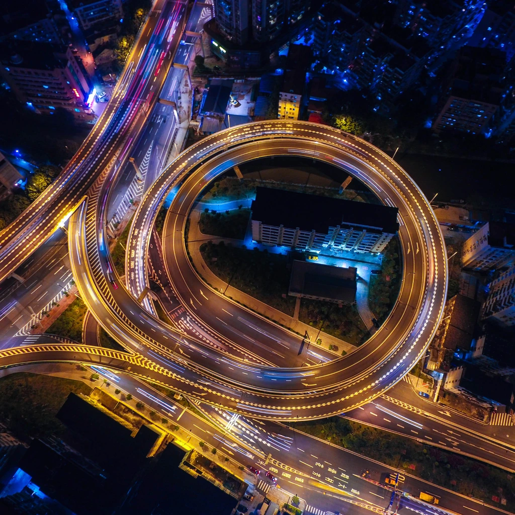 Aerial view of illuminated city roads and a curved highway ramp at night