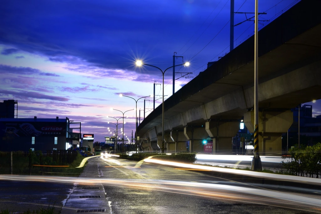 Roadway streetlights beside an elevated railway at dusk.